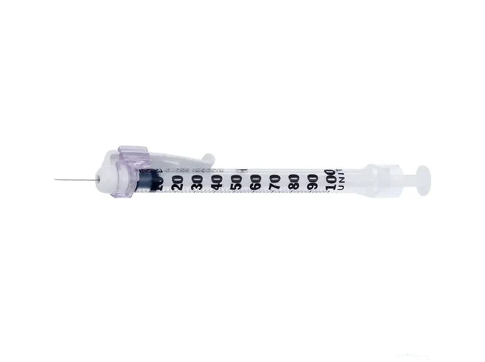 A syringe lies horizontally on a plain white background. The syringe is transparent with black markings along its barrel.
