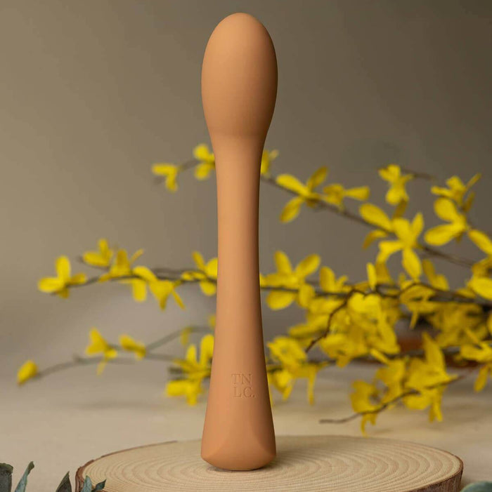 Cecily Curved G-Spot and Wand-Style Vibrator, a sleek curved g-spot vibrator on a wooden base with yellow flowers.