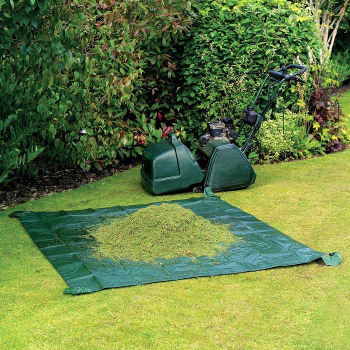A green garden tidy sheet laid on grass with garden waste collected on it, next to a lawn mower.