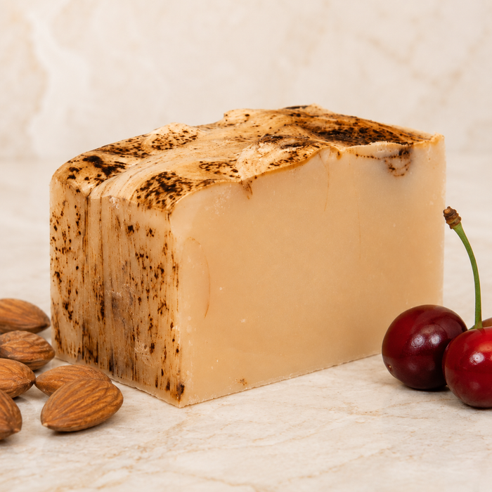 Bar of goat milk soap surrounded by almonds and cherries on a light background