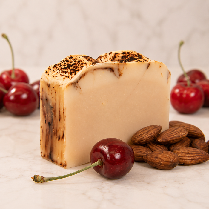 Bar of goat milk soap with dotted surface, cherries, and almonds on a light background