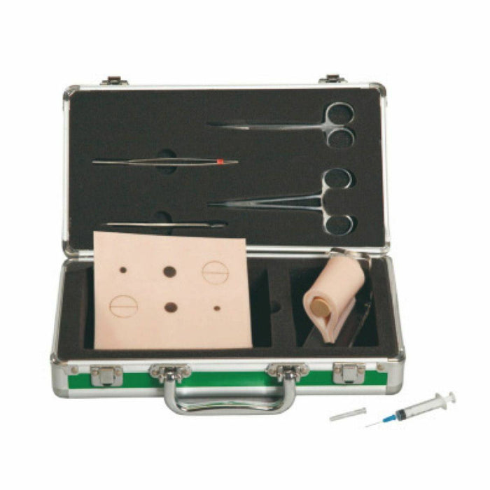 A medical kit rests open, displaying tools such as scissors, forceps, a suture practice pad, and a skin substitute. A syringe and needle are also placed near the kit.