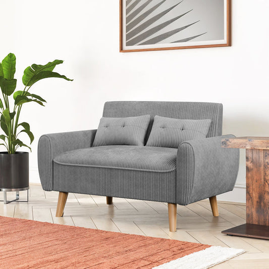Gray sofa with wooden legs in a room with a plant and a rug.