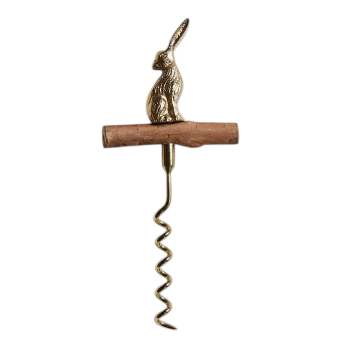 A bottle of wine with a golden foil sits beside the BE HOME - HARE CORKSCREW by BE HOME, INC, featuring a brass rabbit-shaped handle and wooden grip on a light wood surface—an elegant gift for any hostess.
