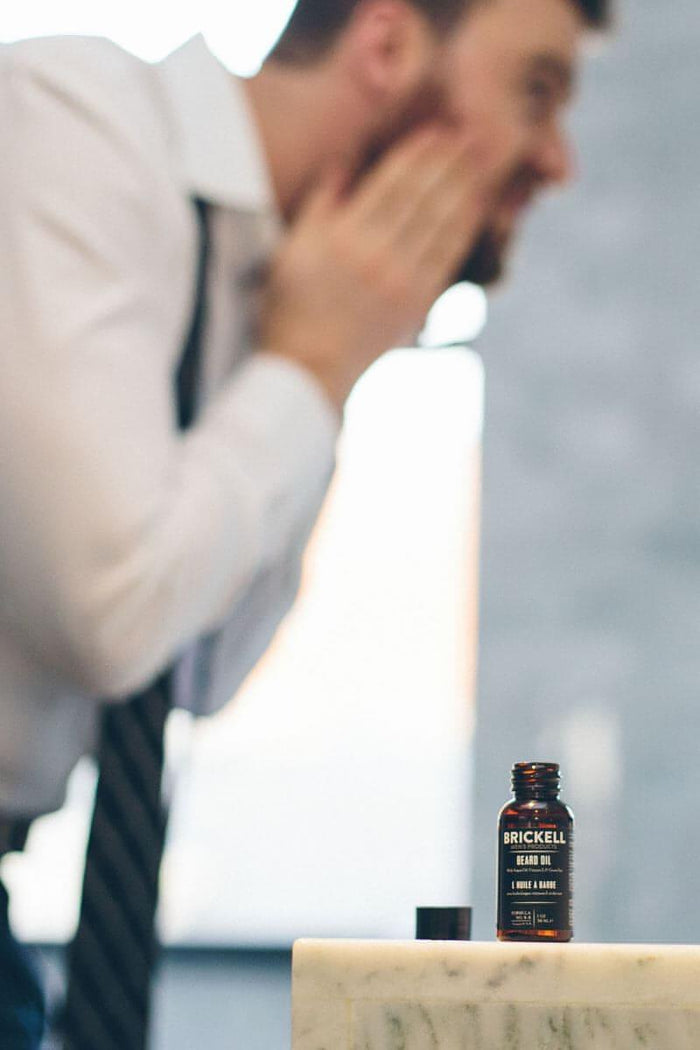 Man applying beard oil in front of a mirror in a bathroom