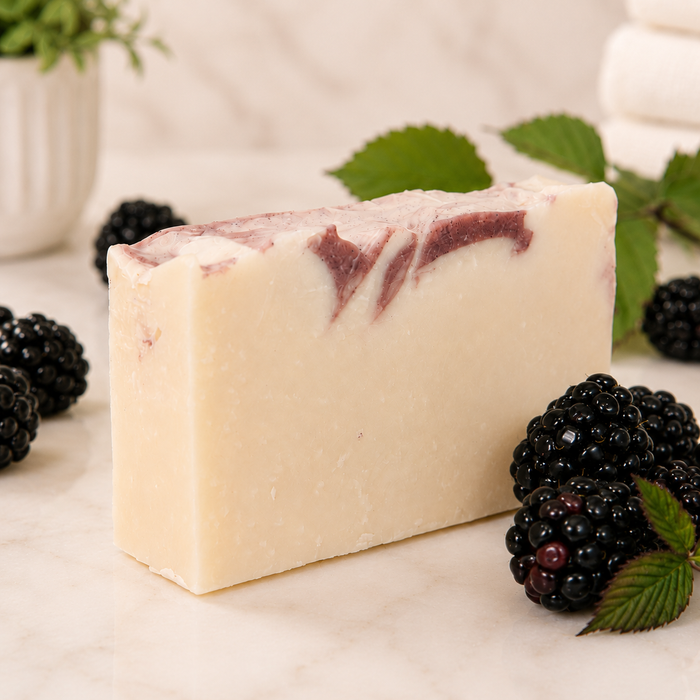 Bar of goat milk soap with blackberry swirls surrounded by blackberries on a light background