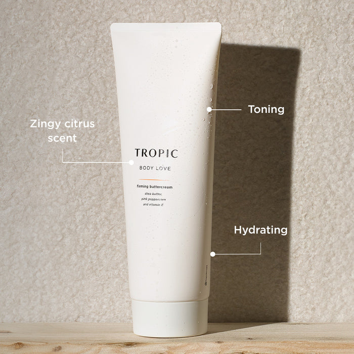 White tube of Tropic Body Love firming buttercream with water droplets on the surface, shown against a textured beige background. Text callouts highlight benefits: “Zingy citrus scent,” “Toning,” and “Hydrating.”