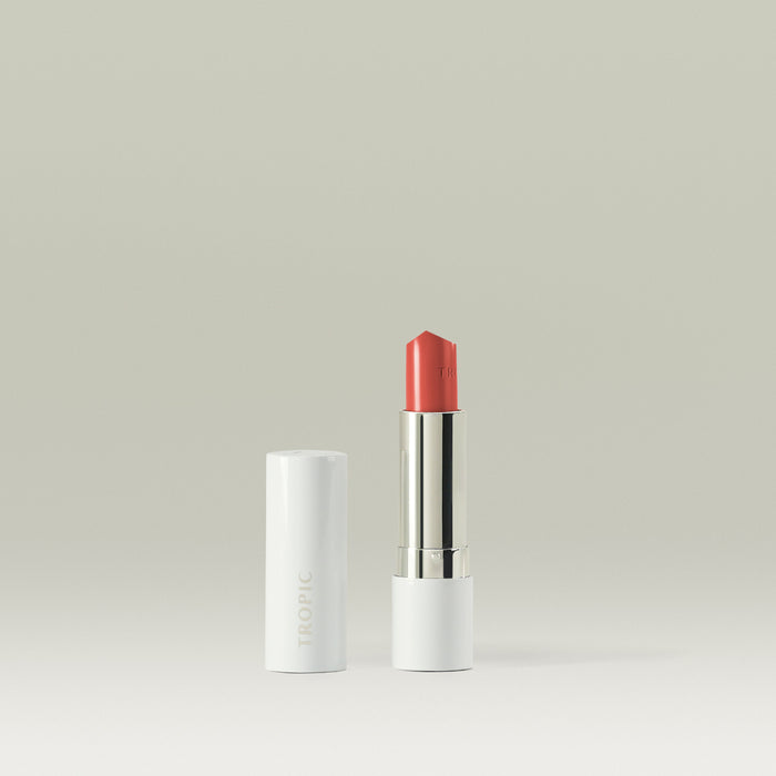 Tropic Butter Tint in a coral shade shown open beside its white casing on a minimal background.