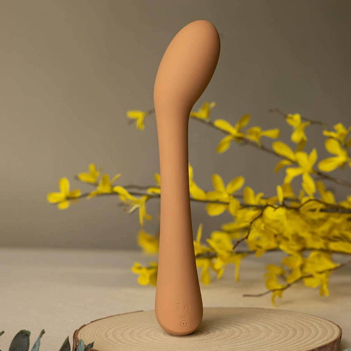 Cecily Curved G-Spot and Wand-Style Vibrator, a sleek curved g-spot vibrator on a natural wood stand surrounded by flowers.