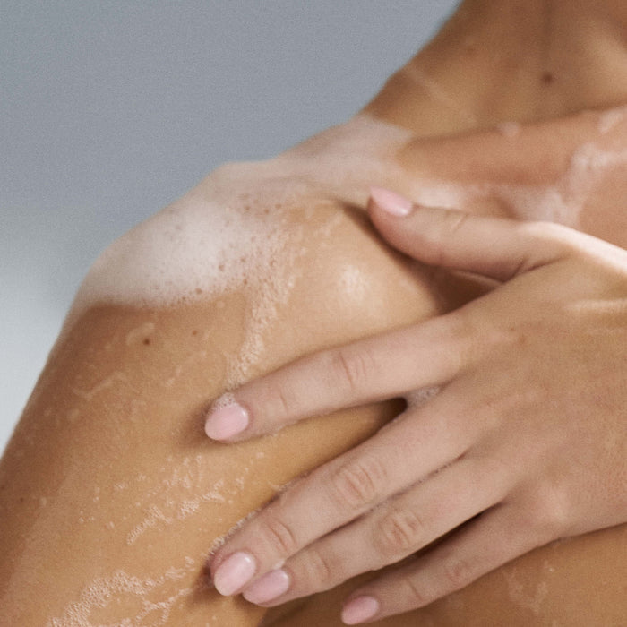 Hand applying a body wash to shoulder against a neutral background