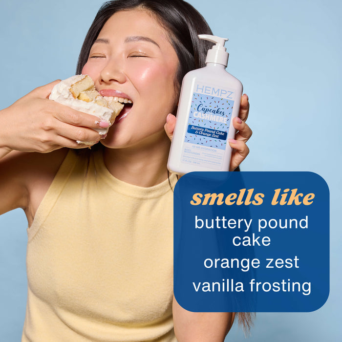 Person eating a donut and holding a bottle of Hempz Cupcakes & Cashmere Moisturizing Body Lotion with a blue background.
