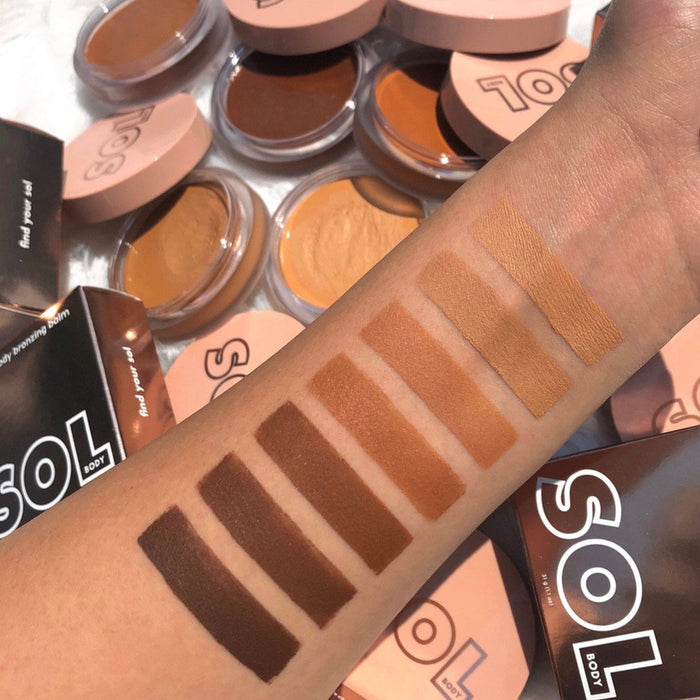 Arm swatches of ColourPop SOL Face & Body Bronzing Balm, including the Dark shade, displaying creamy bronzer stripes from deep espresso to warm tan, with open SOL compacts and blush-pink lids scattered in a flatlay background.