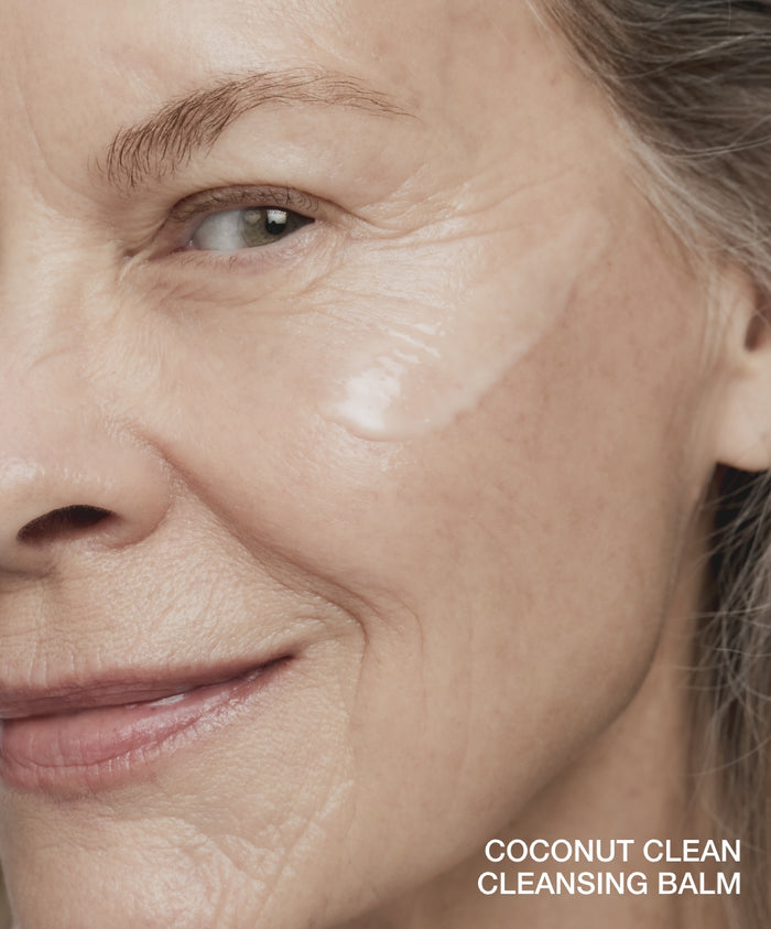 Close-up of a mature woman smiling with a moisturizing cleanser applied on her cheek, highlighting gentle skincare using the Double Clean Cleanser Duo with natural ingredients.