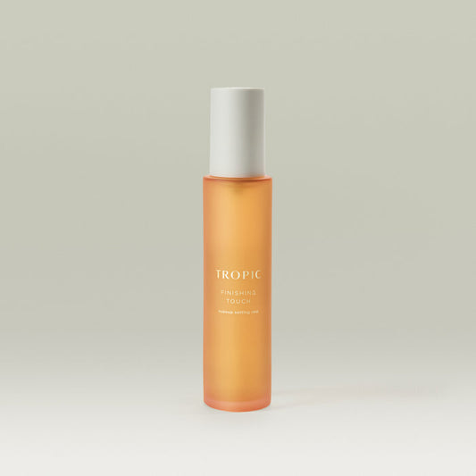 Tropic Finishing Touch makeup setting mist in a sleek orange frosted bottle with white cap, standing upright on a neutral background.