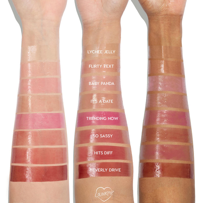 Flirty Text swatch of the ColourPop So Juicy Plumping Glossy Lip Oil gleaming on three forearms, showing a sheer rosy-pink tint and high-shine finish across multiple skin tones, with other shade strips labeled for comparison.