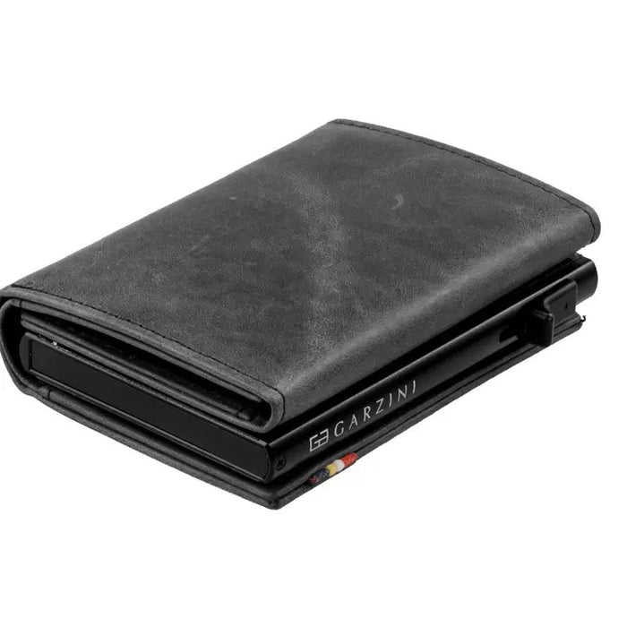 A closed black GARZINI Slim Trifold RFID-blocking leather wallet with metal card holder and coin pocket, showing the brand name on the side and cards partially visible along the edge.
