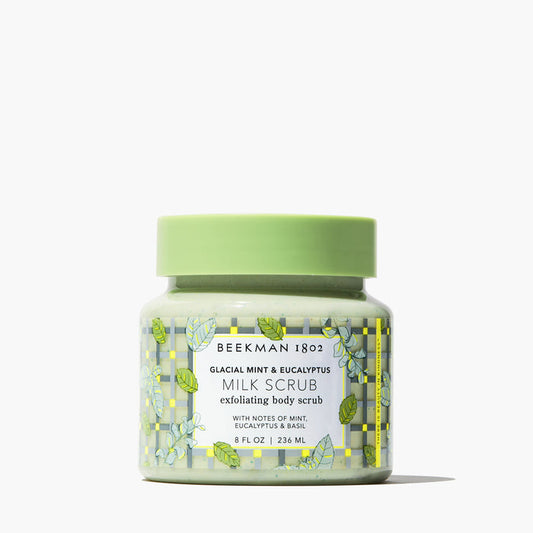 A jar of Beekman 1802 Glacial Mint & Eucalyptus Milk Scrub with a green lid and label featuring botanical designs.