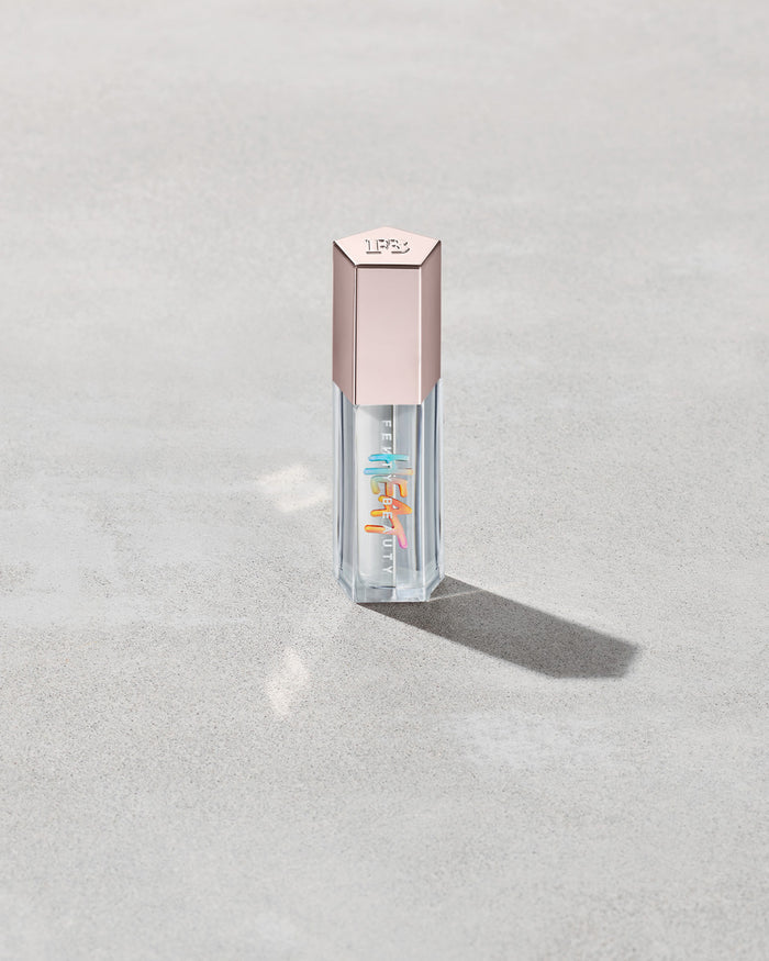 Closed tube of Gloss Bomb Heat lip gloss and plumper in the shade Glass Slipper on a grey background.
