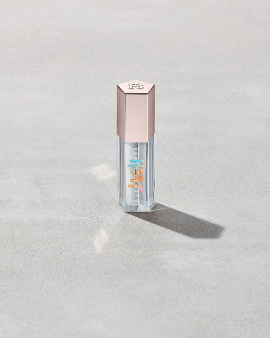 Closed tube of Gloss Bomb Heat lip gloss and plumper in the shade Glass Slipper on a grey background.
