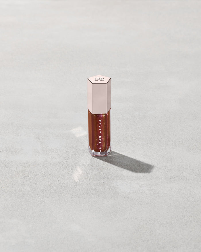 A close tube of Gloss Bomb Universal Lip Luminizer in the shade Hot Chocolit Fantasy on a grey background.