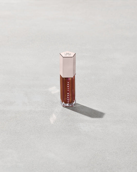 A close tube of Gloss Bomb Universal Lip Luminizer in the shade Hot Chocolit Fantasy on a grey background.