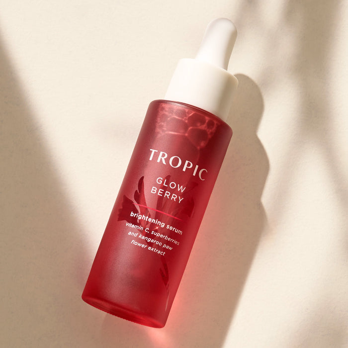 The image shows a red bottle labelled "Glow Berry" with the description "brightening serum" underneath. It mentions key ingredients such as vitamin C, superberries, and kangaroo paw flower extract. The bottle has a white dropper cap, and it is lit with soft shadows for a clean, natural look.