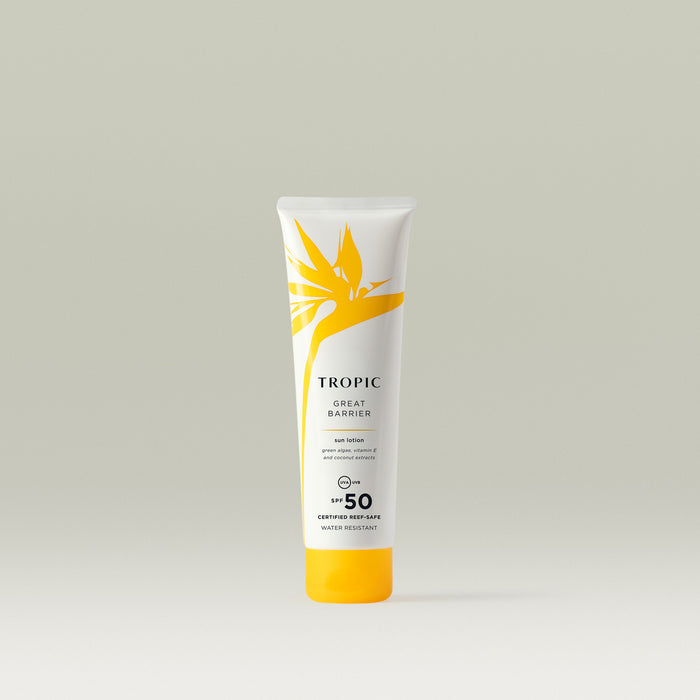 A smaller white tube of Tropic Great Barrier Sun Lotion with SPF 50, decorated with a yellow tropical leaf design and text emphasising 'certified reef-safe' and 'water resistant'.