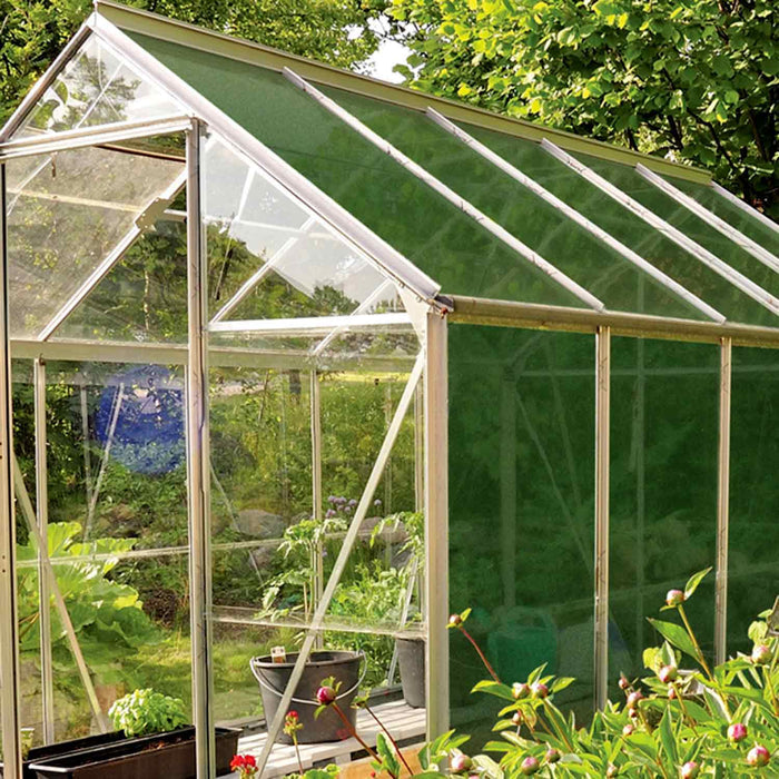 A greenhouse with shading sheet covering roof and side panels. Set in a garden environment.