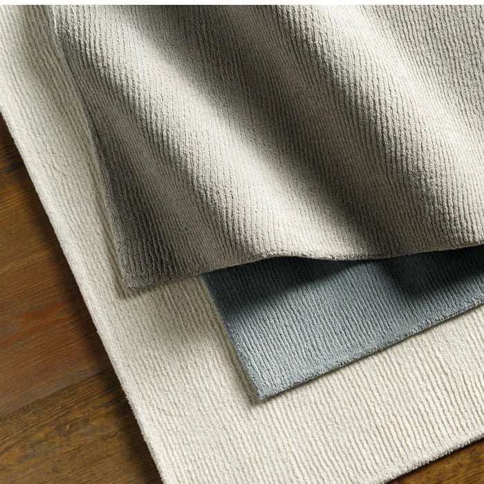 Close-up of textured rug samples in beige, gray, and white on a wooden floor.