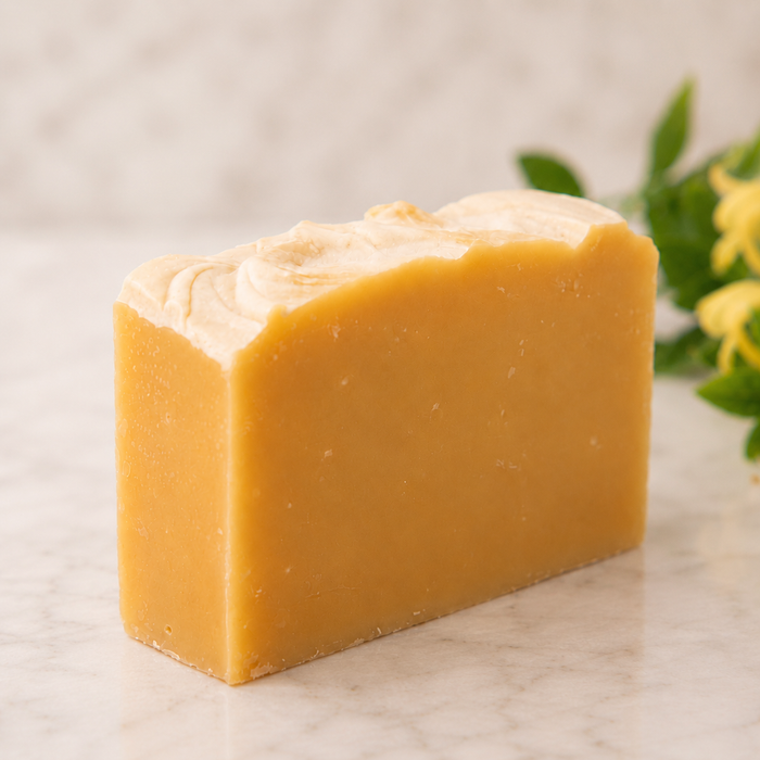 Bar of yellow goat milk soap on a marble surface with greenery in the background
