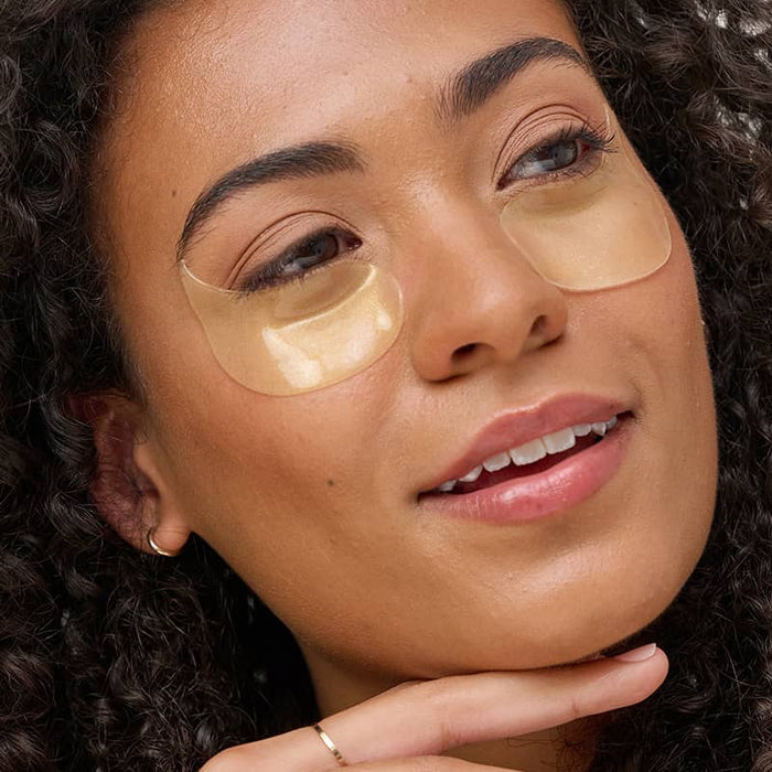 Woman with curly hair wearing gold Patchology illuminating eye gels for a brightened and refreshed undereye appearance.