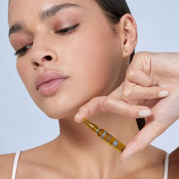 Woman holding ISDIN Isdinceutics Hyaluronic Booster ampoule near face