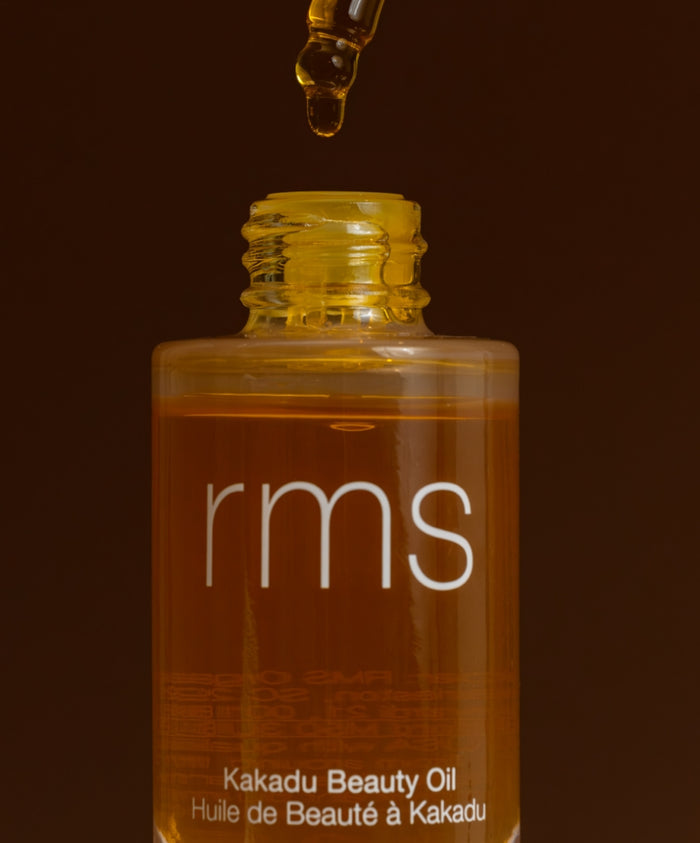 Close-up of a glass bottle of Kakadu Beauty Oil with a dropper releasing golden oil, showcasing natural ingredients and clean beauty skincare by RMS Beauty.