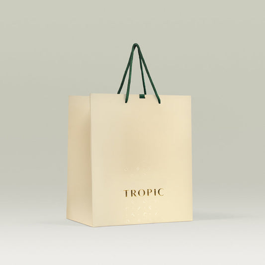 Cream-colored Tropic gift bag with gold logo and dark green rope handles, displayed against a light neutral background.