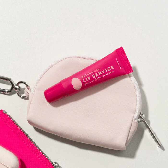 Patchology Lip Service gloss-to-balm treatment tube resting on a light pink zippered pouch for a portable beauty routine.