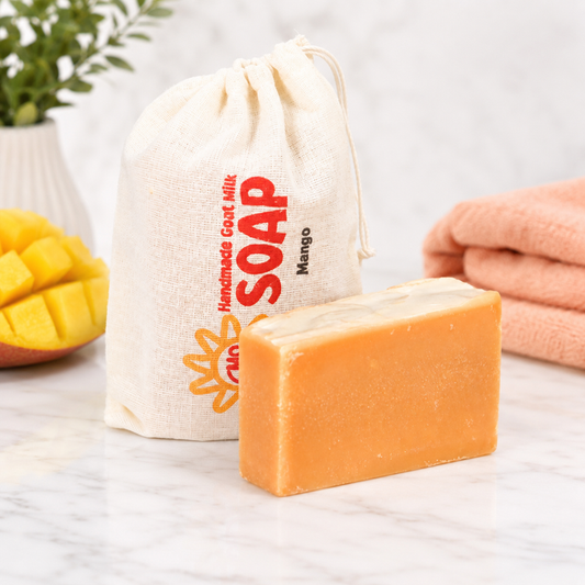 Bar of goat milk soap with a drawstring bag labeled 'Handmade Goat Milk Soap Mango' on a light surface.