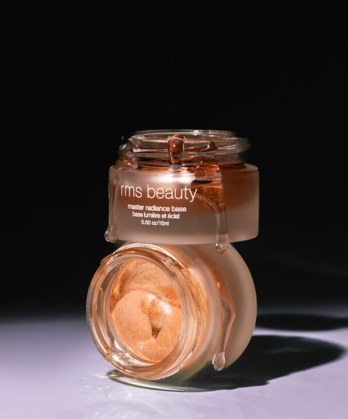 Two open jars of Master Radiance Base by RMS Beauty showing creamy, radiant, rose-gold tinted makeup with a smooth texture, highlighting clean beauty and natural ingredients.