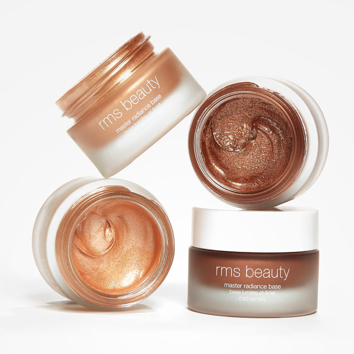Three open jars showing cream makeup in warm copper and bronze tones and a closed jar, all labeled Master Radiance Base by RMS Beauty on a white background