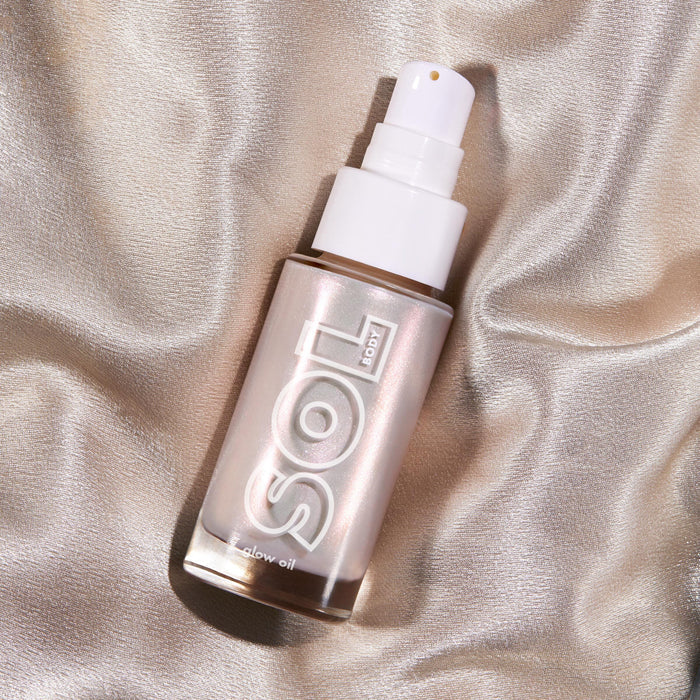 Moonstone SOL Glow Oil bottle tilts on champagne silk, its frosted glass and white pump catching light with a pearlescent glow; ColourPop SOL Glow Oil for luminous body shine in a sleek pump design.