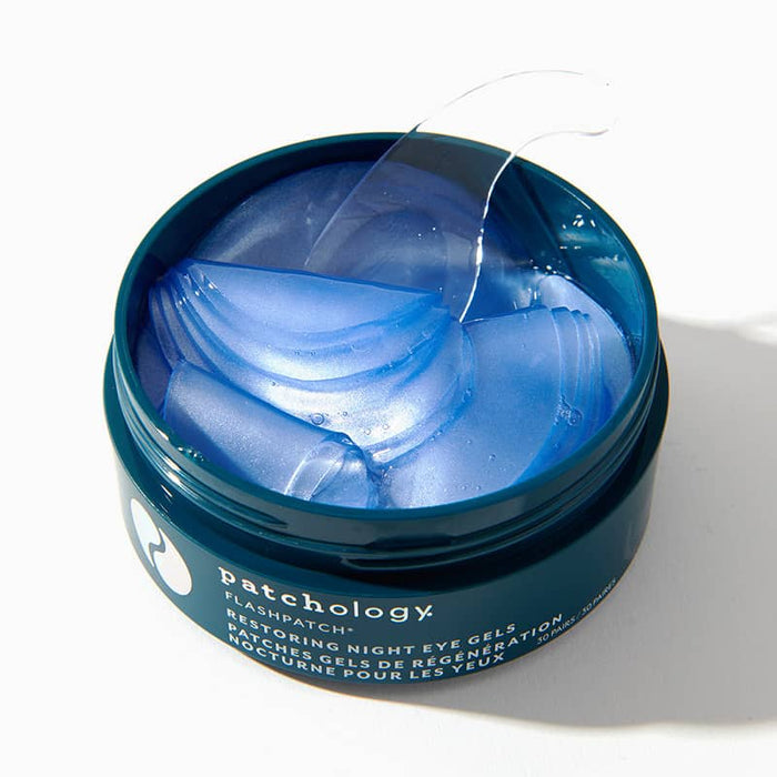 Open jar of blue Patchology FlashPatch Restoring Night Eye Gels with a clear spatula for overnight undereye care.