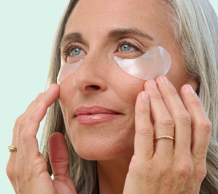 Woman applying eye patches with a light blue background