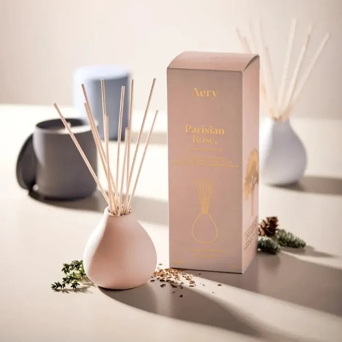 Parisian Rose reed diffuser displayed with packaging and decorative elements on a table.