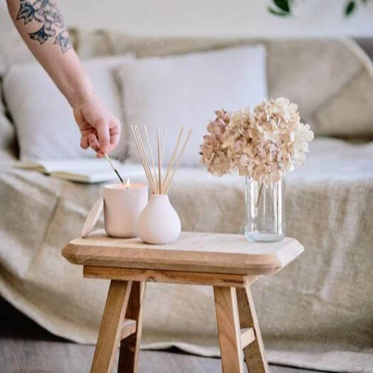 A stylish living room setup featuring a Parisian Rose reed diffuser, a candle, and fresh flowers on a wooden table.