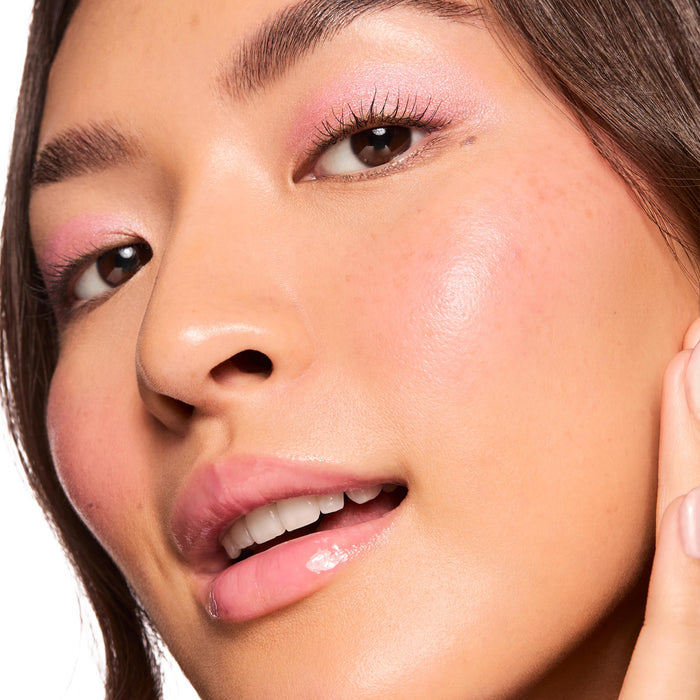 Dewy cheekbone glowing as Pink Pony liquid highlighter catches light, showcasing ColourPop Liquid Highlighter on the high points; soft pink eyeshadow and glossy lips complete the look in a close-up beauty macro against a white background.