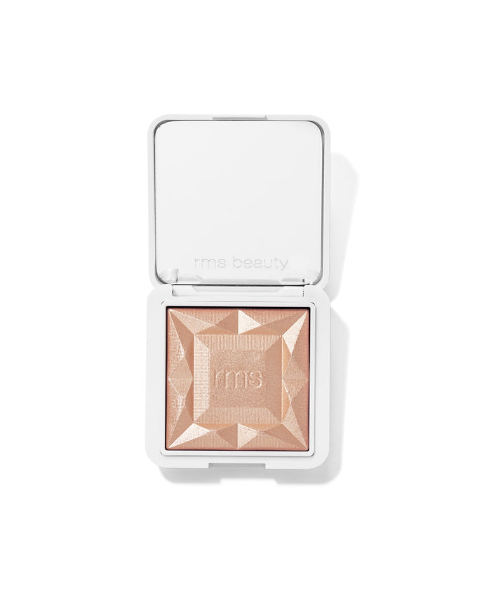 Compact highlighter with a faceted design in a light champagne shade, featuring the brand RMS Beauty embossed, for a radiant glow called ReDimension Hydra Dew Luminizer.