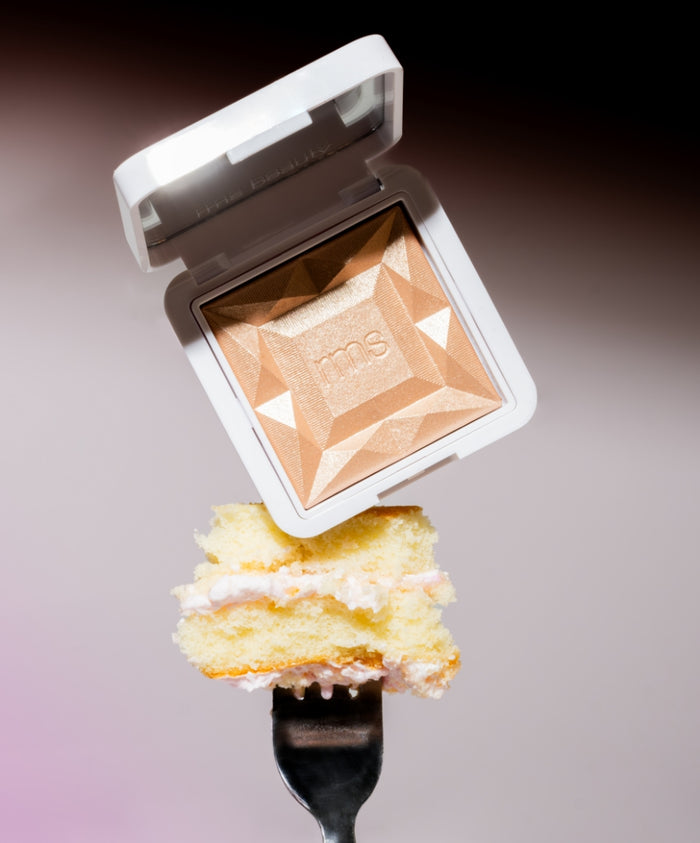 Open compact of ReDimension Hydra Dew Luminizer with a geometric pattern, hovering above a fork holding a piece of yellow cake with white frosting.