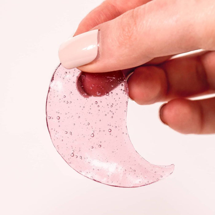 Hand holding a translucent pink hydrogel eye patch filled with tiny bubbles, showcasing its cooling and jelly-like texture for a hydrating skincare routine.