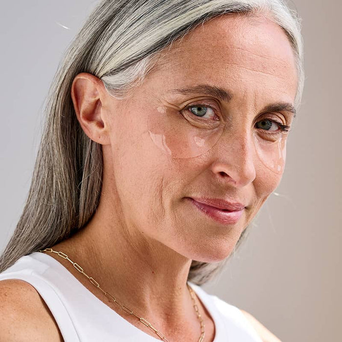 Mature woman with grey hair wearing clear Patchology eye gels for a revitalized and refreshed under-eye appearance.