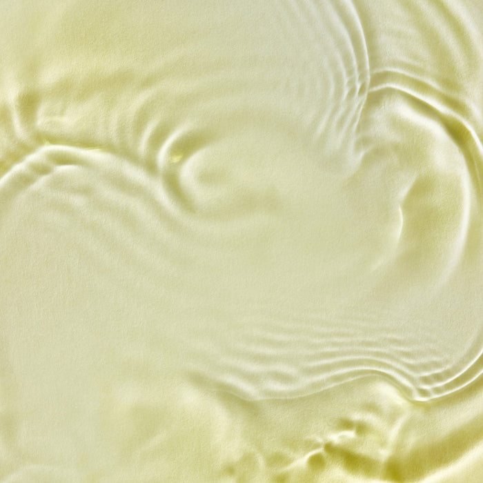 Close-up of Tropic Signature Oil’s silky golden texture with soft ripples and light reflections.