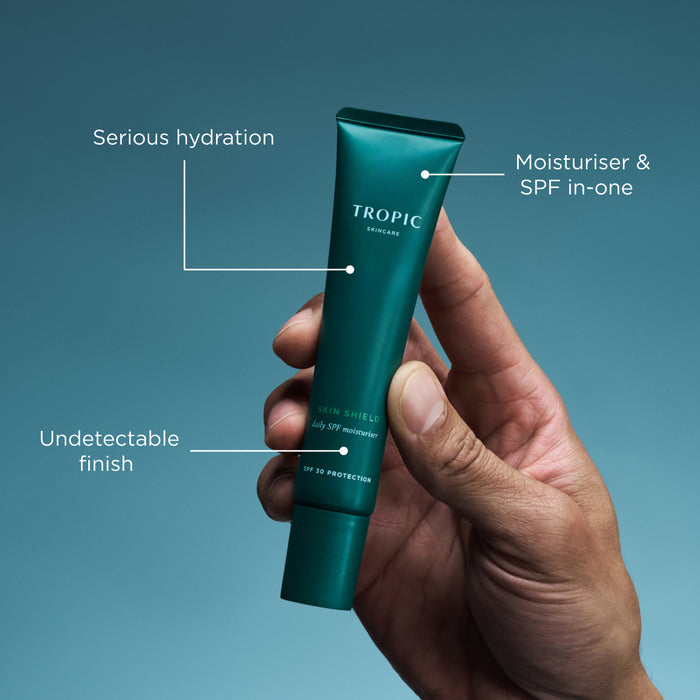 Hand holding Tropic Skin Shield SPF moisturiser tube with hydration and SPF benefit callouts.